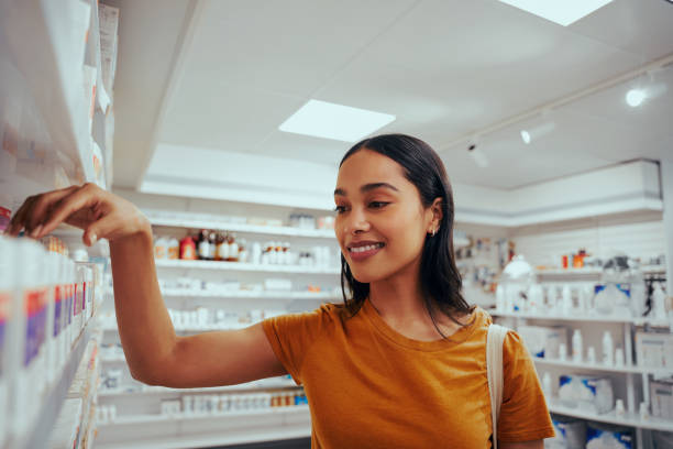 porträt einer lächelnden jungen frau in drogerie stehen gegen regal picking medizin - shelf pharmacy people indoors stock-fotos und bilder