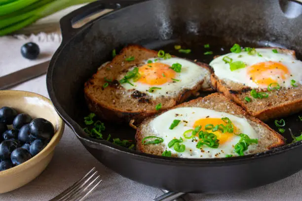 Rustic breakfast with fried eggs in a whole made with fresh rye bread and served with blueberries on a wooden table