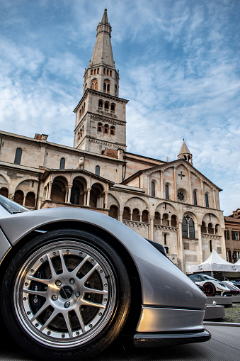 Modena, Italy - May 17, 2019: Wheel of a Pagani sports car with the Modena Cathedral and the Ghirlandina Tower in the background, in Piazza Grande, during the Motor Valley Fest.