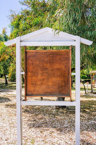 Old  information stand with empty scratched brown wooden board in a park under the tree. Summer cafe menu mock up