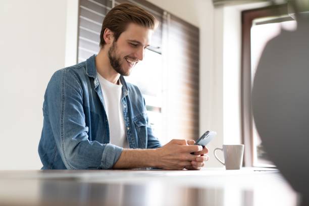 istock Confident man holding smartphone, sitting in kitchen, chatting online with friends or colleagues, browsing app 1323681253
