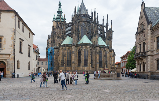 Prague, Bohemia Czech Republic, may 20th 2017, a medium group of tourists (walking, standing, sitting, photographing) on the courtyard in front of the Western facadel of the St. Vitus Cathedral in Prague (Katedrála svatého Víta, Václava a Vojtěcha) - the construction of the Gothic Roman Catholic metropolitan cathedral began in 1344, it is located entirely within the Prague Castle complex (Pražský hrad) - Prague is considered to be one of the most beautiful cities in Europe and is a popular travel destination for tourists