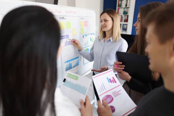 istock Woman coach standing at blackboard and showing documents with graphs to students 1323683596