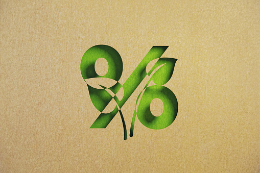 Cut out leaf shaped made of recycled paper intersect with percentage sign on green background. Horizontal composition with copy space. Sustainability concept.