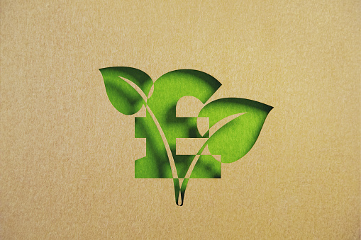 Cut out leaf shaped made of recycled paper intersect with pound symbol on green background. Horizontal composition with copy space. Sustainability concept.
