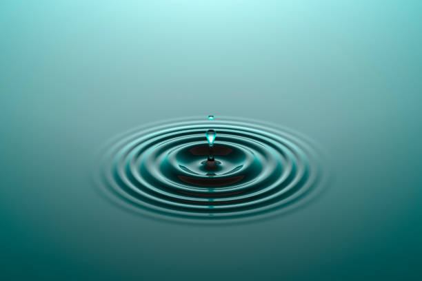 Water drop falling into water surface with ripples stock photo