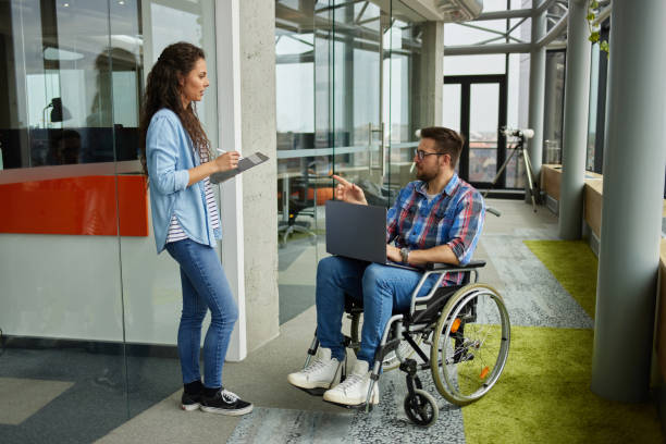 istock Disabled male computer programmer discussing with female coworker in office hallway 1323690151