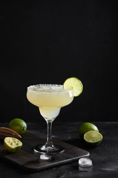istock Classic Margarita cocktail with lime juice and ice cube on black background. Vertical orientation. 1323694714