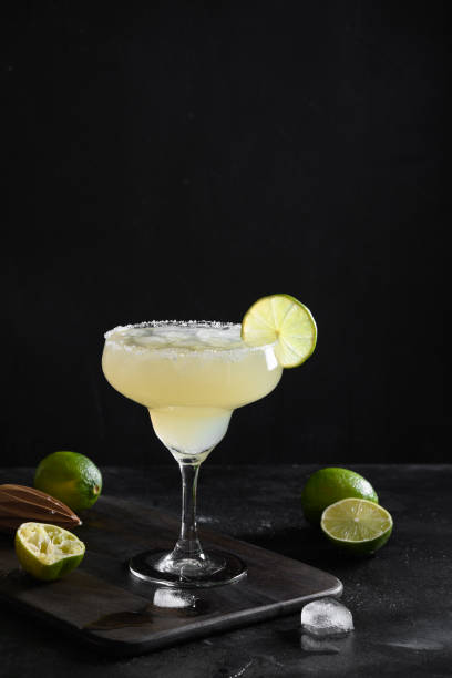 Classic Margarita cocktail with lime juice and ice cube on black background. Vertical orientation. Classic Margarita cocktail with lime and ice cube on black background. Vertical format. Freshness summer alcoholic beverage. margarita stock pictures, royalty-free photos & images