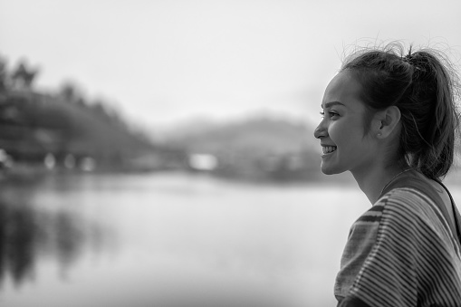 A monochrome image of a 40 something black woman turning to laugh at the camera. She is on a grey background and is wearing trousers and a long sleeved white top.  Her hands are in her pockets. Her hair is black, straight and long.