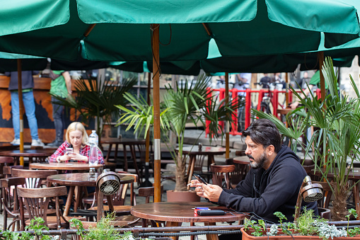 Lviv, Ukraine - May, 2021: People sitting in outdoor cafe and looking in smartphones