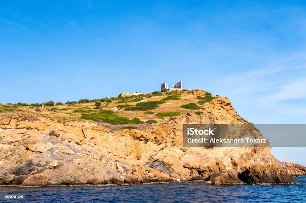 Ancient ruins of Temple of Poseidon on the cliff, Sounion - distant view from the sea in sunny summer day, with crystal blue sky, Greece Sea Stock Photo