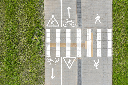 white bicycle road marking on gray tiled pavement. green grass background. aerial top view.