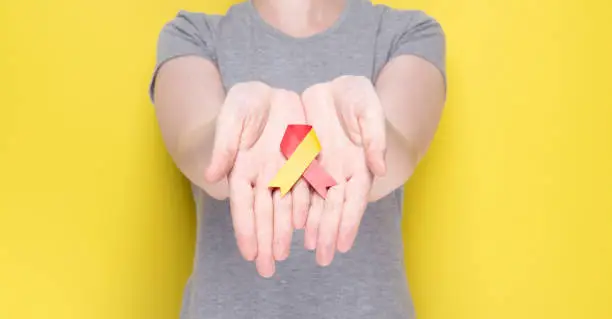 World Hepatitis Day concept. Girl in gray T-shirt holds in her hands awareness symbol red-yellow ribbon. Yellow background