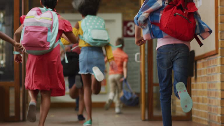 Diverse group of schoolchildren wearing backpacks, running fast through school corridor