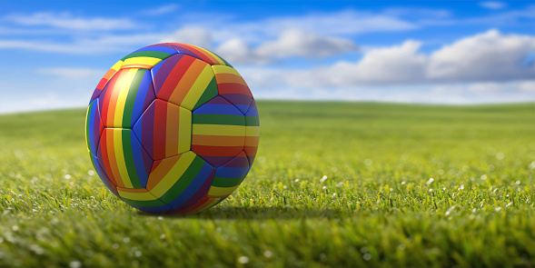 LGBT colors football ball on grass, blue sky background, Gay pride rainbow soccer flag ball, copy space, card tempalte. 3d illustration