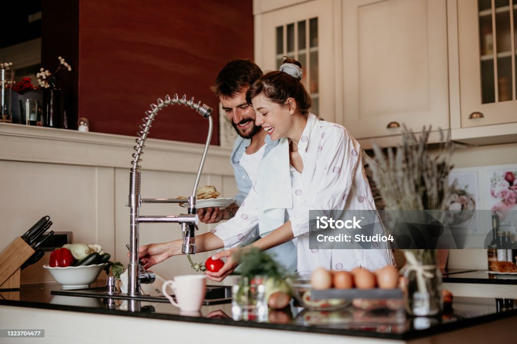 Couple helping each other while cooking Shot of a young woman embracing her partner while he cooks breakfast, Both making breakfast before going to work. 30-34 Years Stock Photo