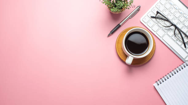 istock Top view of pink workspace with coffee keyboard notebook glasses copy space paste flat. 1323705337