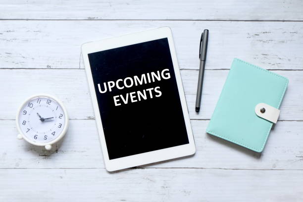 istock Top view of table clock,pen,notebook, and tablet computer written with 'UPCOMING EVENTS' on white wooden background. 1323714295
