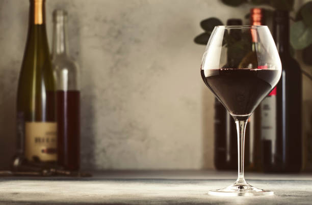 ассортимент вин. красное вино в бокале и бутылки на сером фоне. винный бар, магазин, дегустационная концепция - wine bottle wine rustic liquor store стоковые фото и изображения