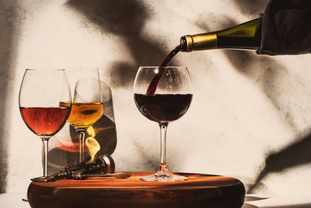 ワインテイスティング。赤ワインは、グラスに赤、白、バラのワインの選択と背景にガラスに注ぎます。硬い日光と葉からの影 - ワイン ストックフォトと画像