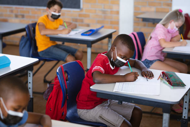 istock African american boy wearing face mask studying while sitting on his desk in the class at school 1323715360