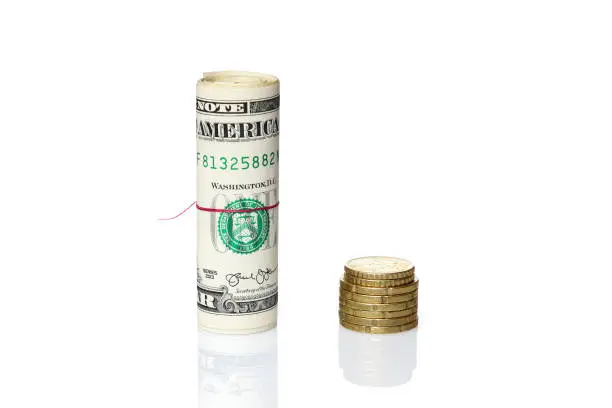 Roll of American dollars next to Euro-coins. Exchange and inequality currency, concept isolated on white background