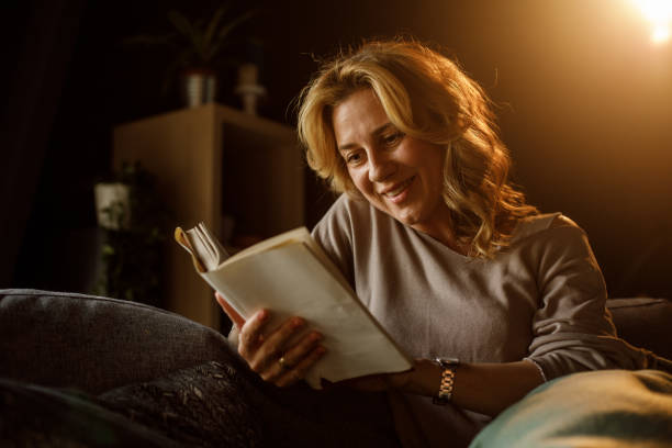 istock Smiling woman reading a book while relaxing on sofa late at night 1323731493