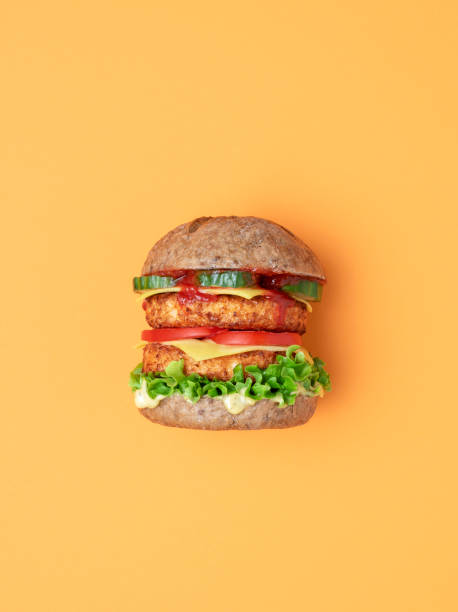 Veggie burger top view isolated on an orange background. Side view from above with a vegan burger on an orange table. Homemade burger with soya patties as a meat substitute, vegan cheese and remoulade, and fresh vegetables. veggie burger photos stock pictures, royalty-free photos & images