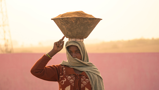 Dumka, Jharkhand, India - November 24 2020: Indian woman worker holding raw material container on the head during work at the construction site