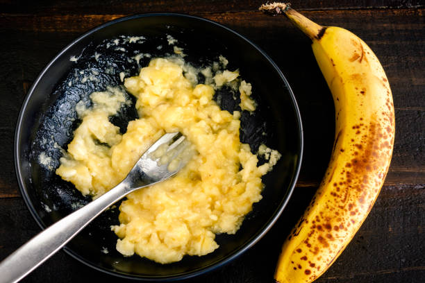 Mashing a Ripe Banana with a Fork A bowl of mashed banana with a whole banana next to it mash food state stock pictures, royalty-free photos & images