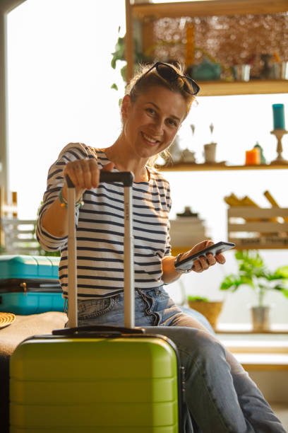 istock Cheerful woman holding her suitcase by it's handle and smiling at camera 1323735507