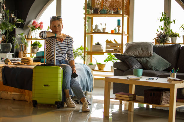 istock Woman sitting on bed, leaning against suitcase handle and contemplating 1323735589
