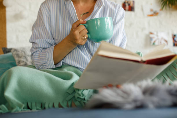 istock Unrecognizable woman reading a book in bed while enjoying coffee 1323736323
