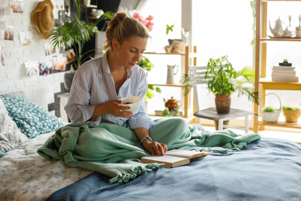 istock Woman enjoying a bowl of cereal in bed while reading a book 1323736786