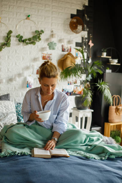 istock Front view of woman having breakfast in bed while reading a book 1323736823