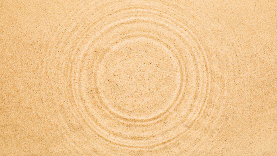 Water rings on water surface over sand. Summer texture background with round copy space.