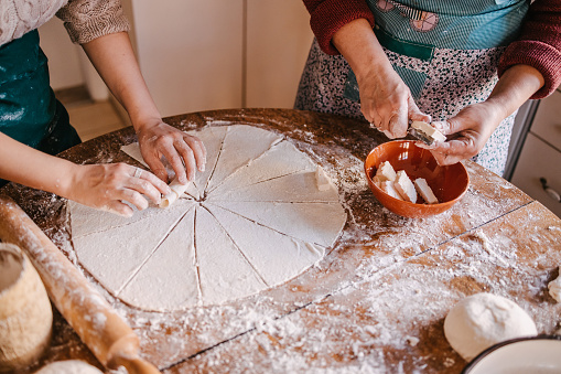 Daughter rolling the cut dough into crescent rolls while mother is cutting butter to grease them