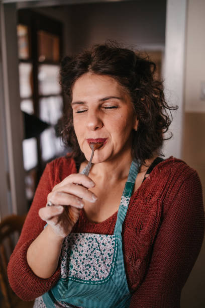 Woman licking the spoon with chocolate cream A middle-aged woman with the apron on licking a spoon with chocolate cream with her eyes closed sugar food stock pictures, royalty-free photos & images
