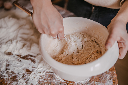 Close-up of a woman's hand mixing dough with the wooden spoon in the plastic bowl