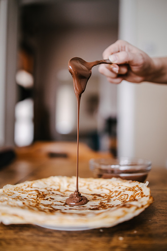 Nutella cream spread dripping from the spoon on the homemade thin crepe pancakes