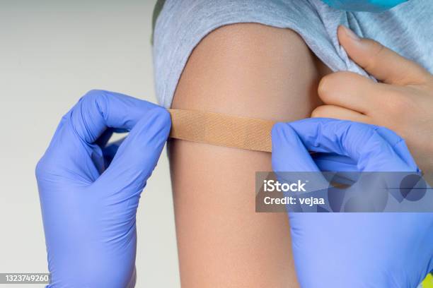 Nurse In Rubber Protective Gloves Putting Bandage Plaster On Teenager Arm After Vaccination Injection Covid Vaccine Stock Photo - Download Image Now