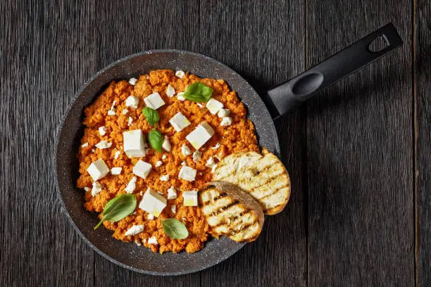 Strapatsada, eggs scrambled with tomatoes and feta cheese in a skillet with toasted bread, horizontal view, greek cuisine, close-up, flat lay, free space