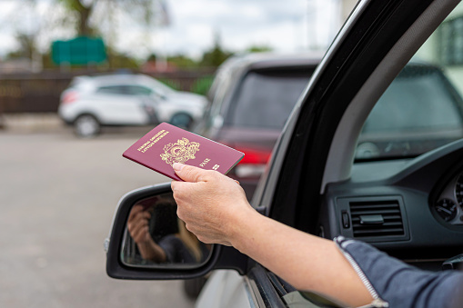 women hand through car window giving passport for customs control, driver with an identity card in a car at a border checkpoint