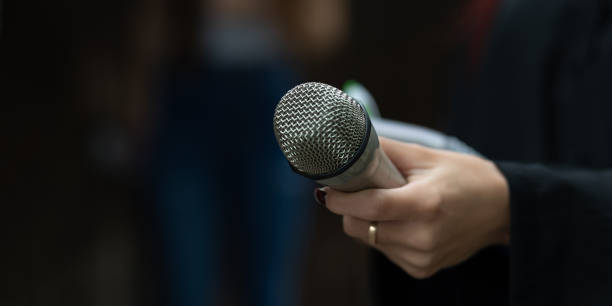 istock Journalist in action at news conference, writing notes, holding microphones 1323756488