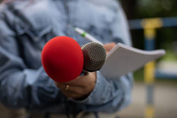 istock Journalist at news conference, writing notes, holding microphones 1323756713