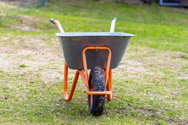 Photo of wheelbarrow closeup on a lawn in garden, garden maintenance, work in garden