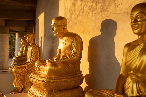 A closeup of an Ancient golden Buddha sculpture on front of a black wall