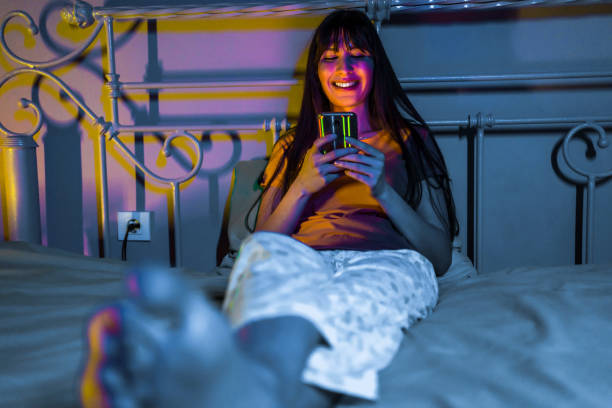 istock Smiling woman using smartphone in bed 1323760612