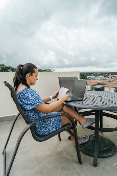 istock Young woman using laptop and tablet while sitting on balcony 1323763976